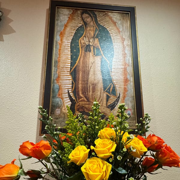 Framed Virgin of Guadalupe artwork with a bouquet of yellow and orange roses in the foreground.