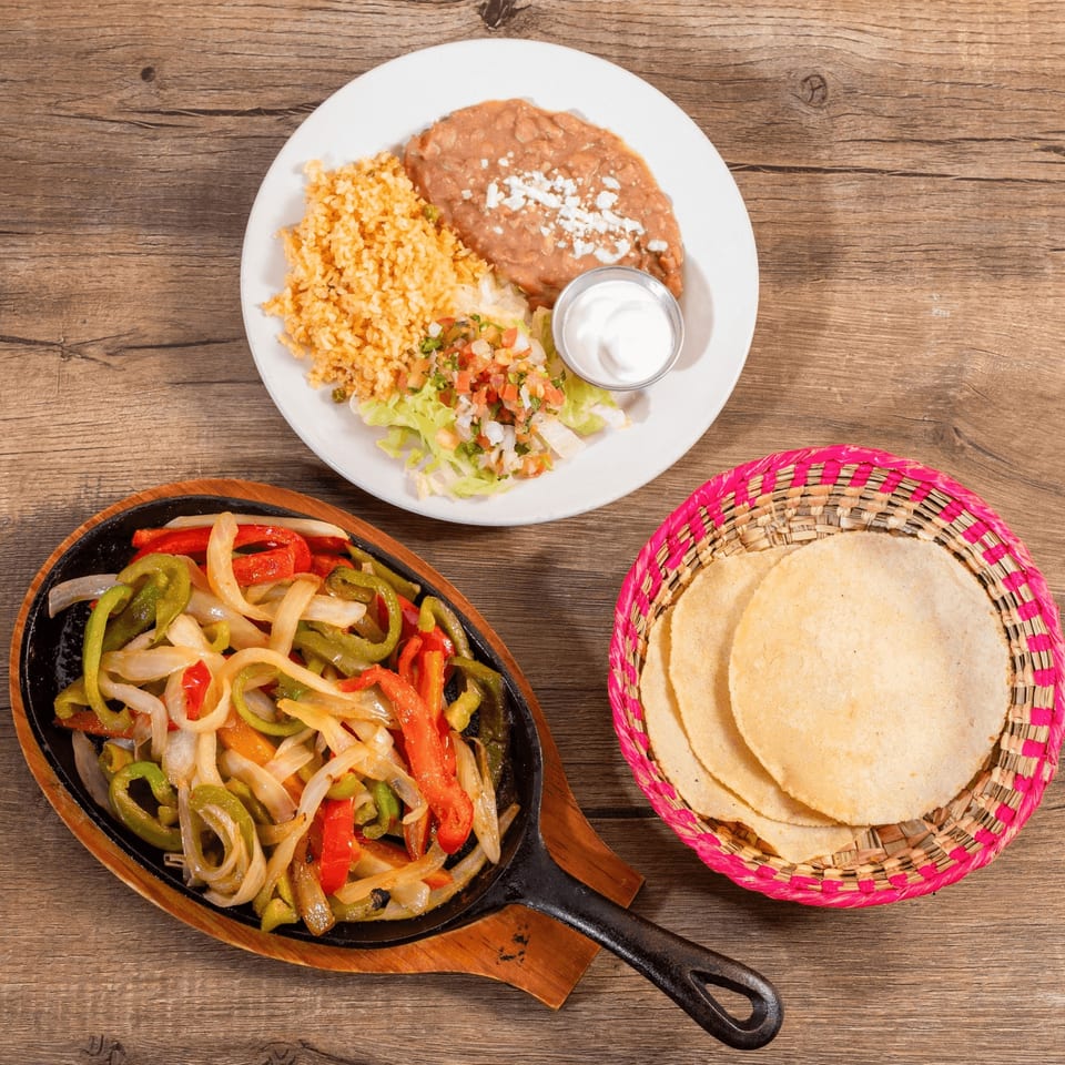 Don Julio's Mexican fajitas with colorful bell peppers and onions, served with rice, beans, and tortillas.
