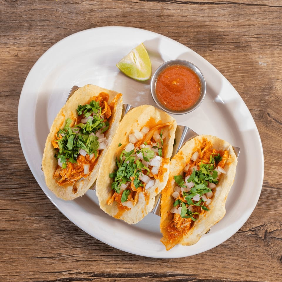 Three Don Julio's chicken tacos with cilantro and onions, served with salsa and lime.