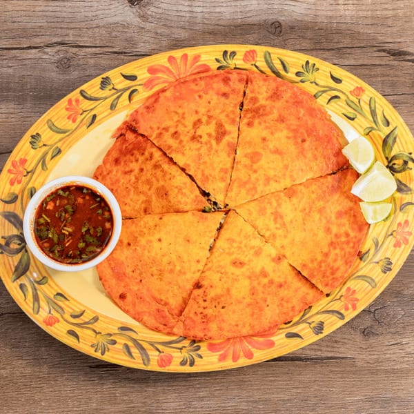 Don Julio's birria quesadilla, cut into six slices, with a side of consommé and lime wedges.
