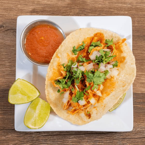 Don Julio's chicken tostada with salsa, cilantro, onions, and lime wedges on a white plate.