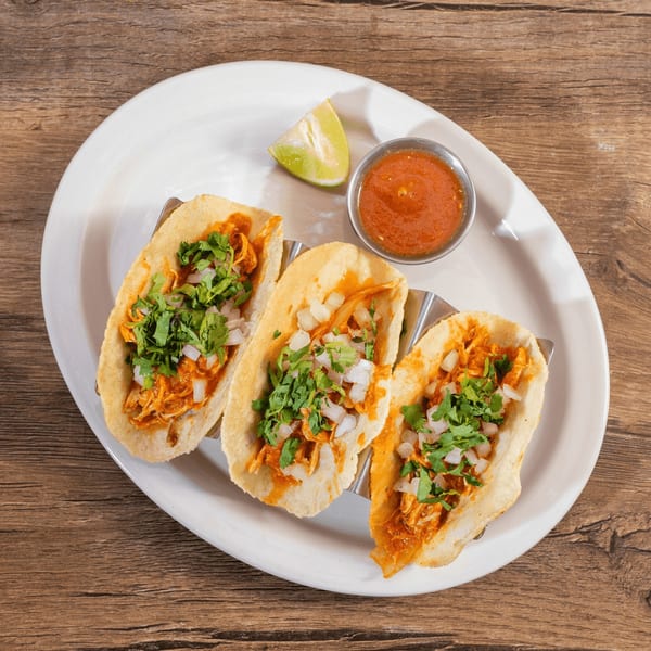 Three chicken tacos with cilantro and onions, served with salsa and lime on a white plate.