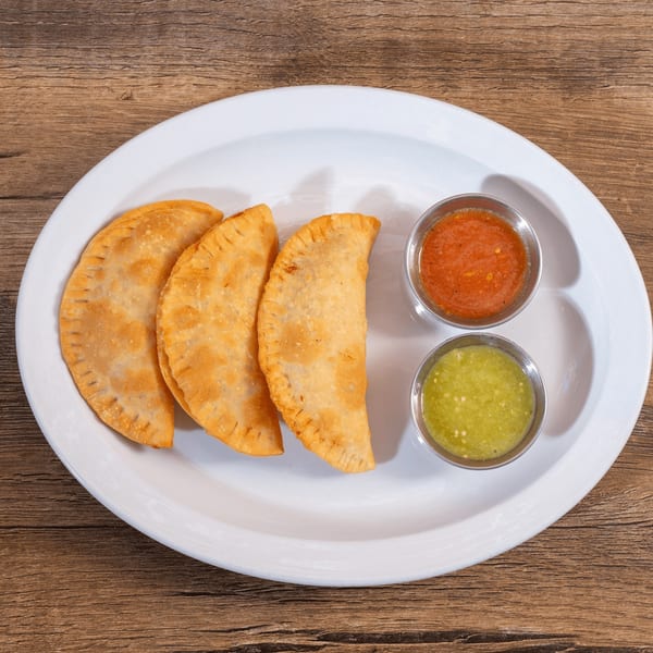 Three golden-brown empanadas with crimped edges, served with red and green salsa on a white plate.