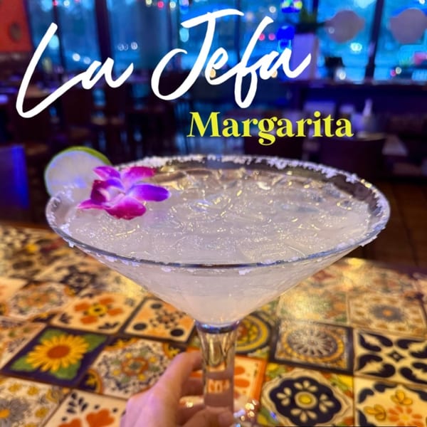 A Don Julio's La Jefa Margarita with a lime and purple flower garnish on a colorful tiled table.