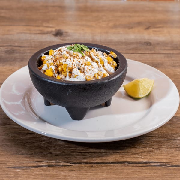 Don Julio's Mexican street corn in a black bowl with crema, chili powder, cilantro, and lime.