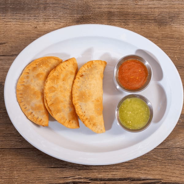 Three golden-brown empanadas with red and green salsa on a white plate.