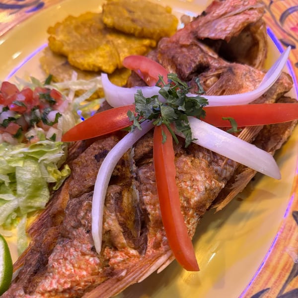 Whole fried fish garnished with onions, tomatoes, and cilantro, served with plantains and salad.