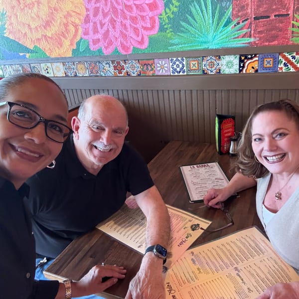 Three smiling people at Don Julio's Mexican restaurant, looking at menus with a colorful mural behind them.