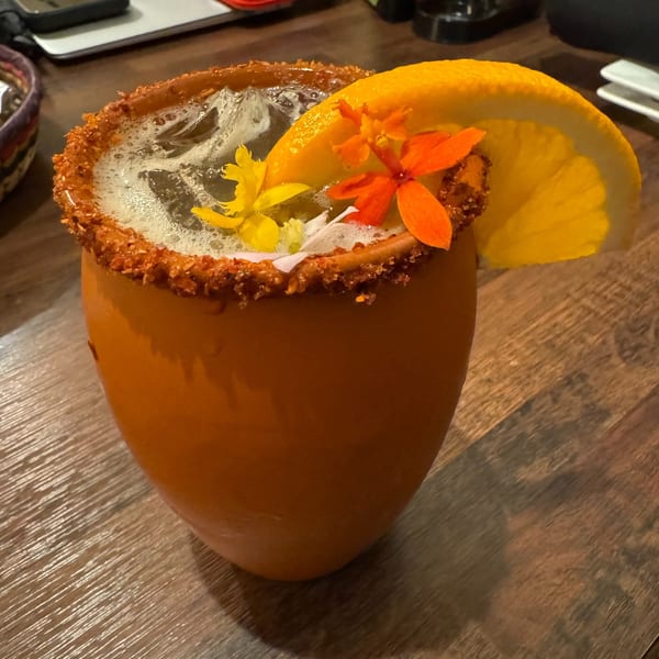 A Don Julio's Mexican drink in an orange mug, garnished with an orange slice and colorful flowers.