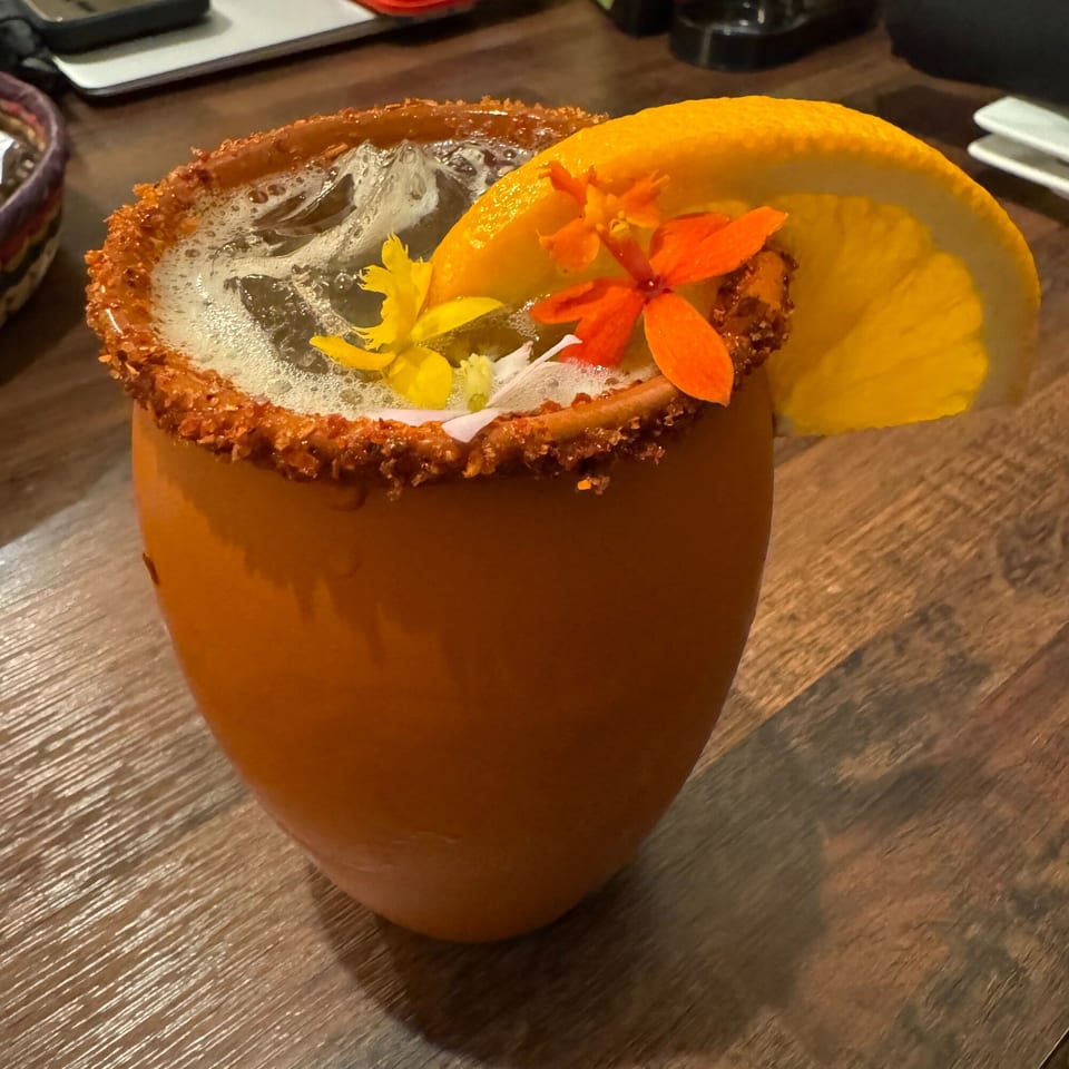 A Don Julio's Mexican drink in an orange mug, garnished with an orange slice and colorful flowers.