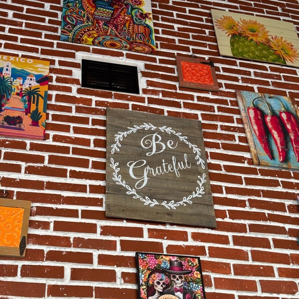 A brick wall adorned with various colorful Mexican-themed art pieces and a "Be Grateful" sign.