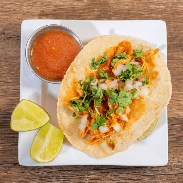 Don Julio's chicken tostada with salsa and lime wedges on a white plate.