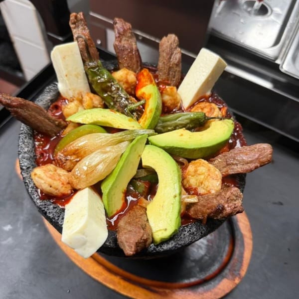 Don Julio's molcajete with steak, shrimp, avocado, cheese, and grilled peppers in a rich red sauce.