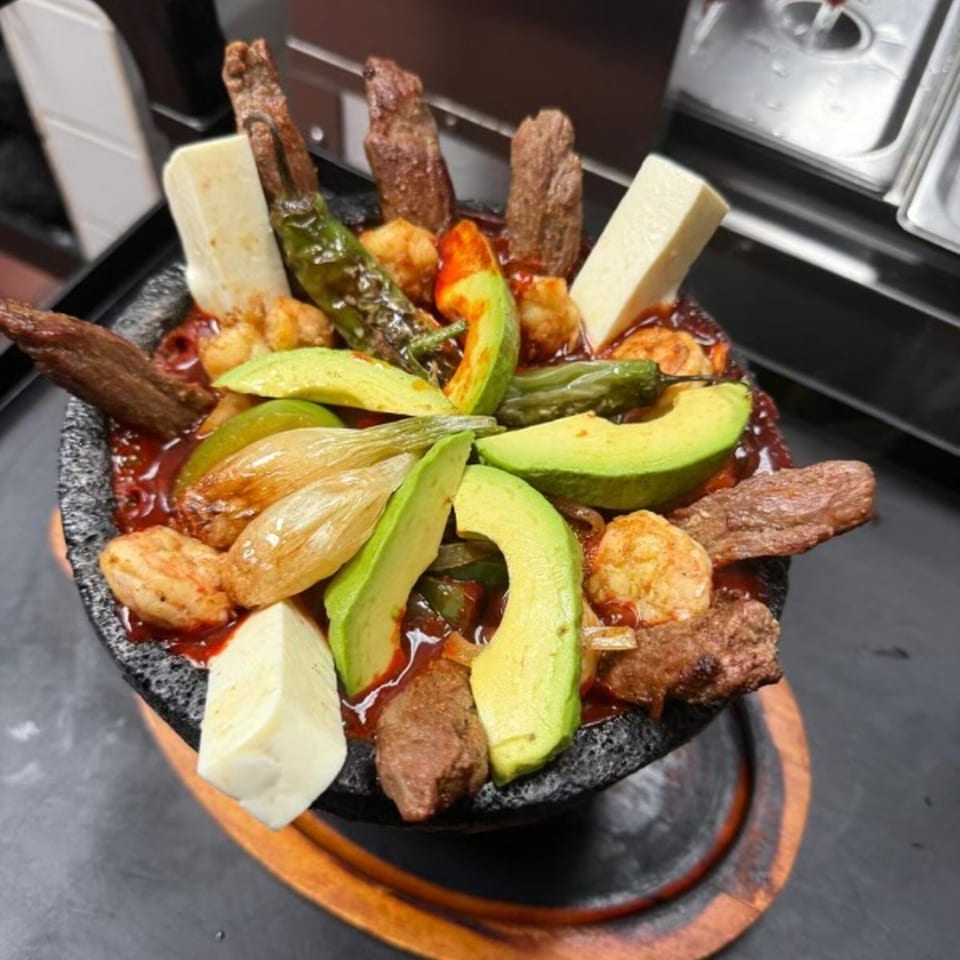 Don Julio's molcajete with steak, shrimp, avocado, cheese, and grilled peppers in a rich red sauce.